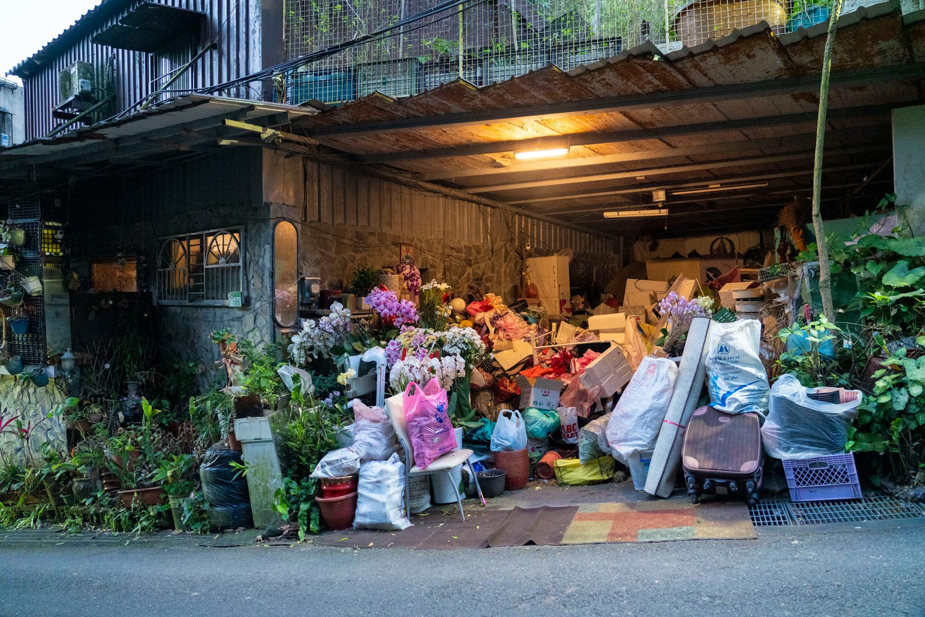 A garage filled with various household items, plants, and clutter overflowing onto the street.