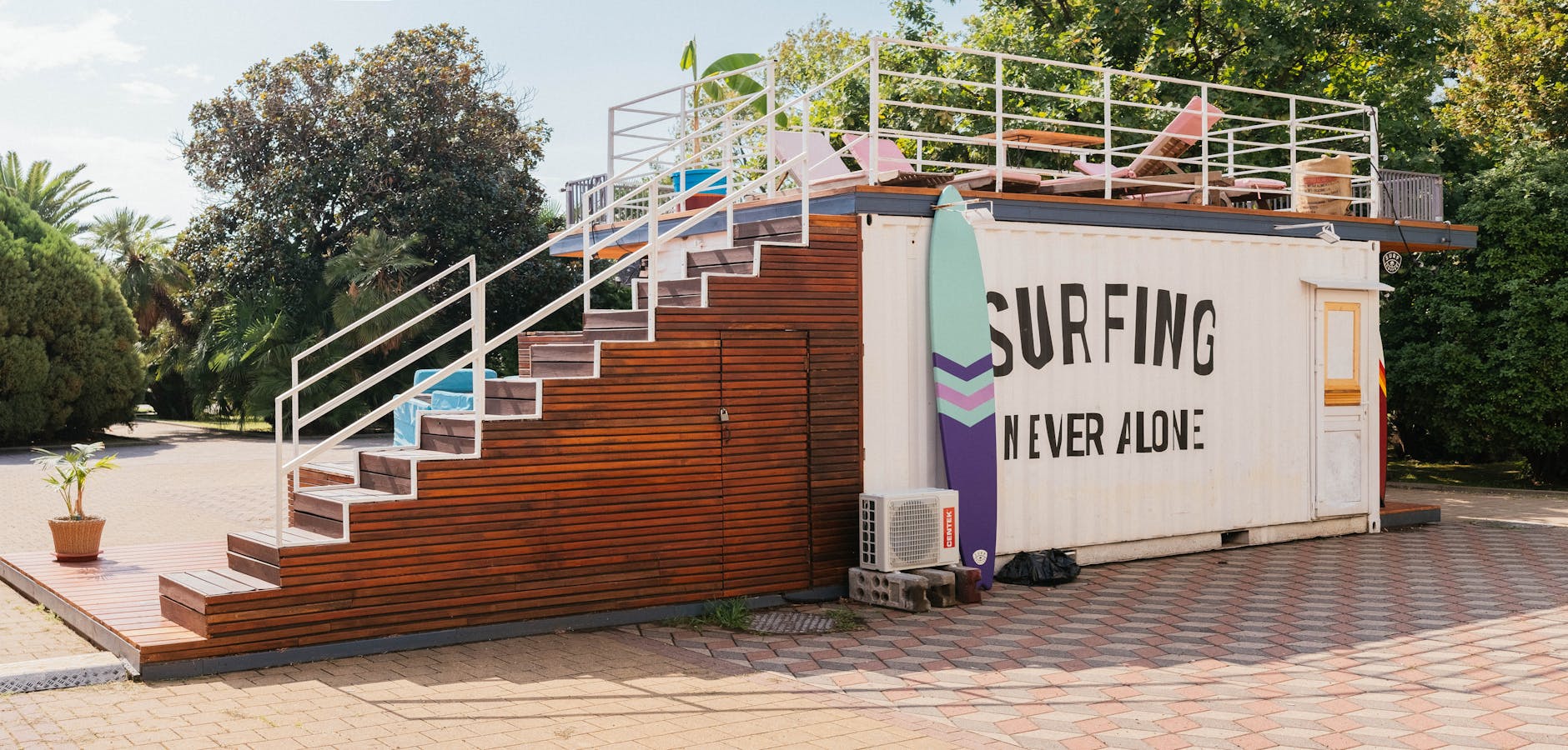 A sunny outdoor scene featuring a surf shack with stairs and colorful surfboard beside it.