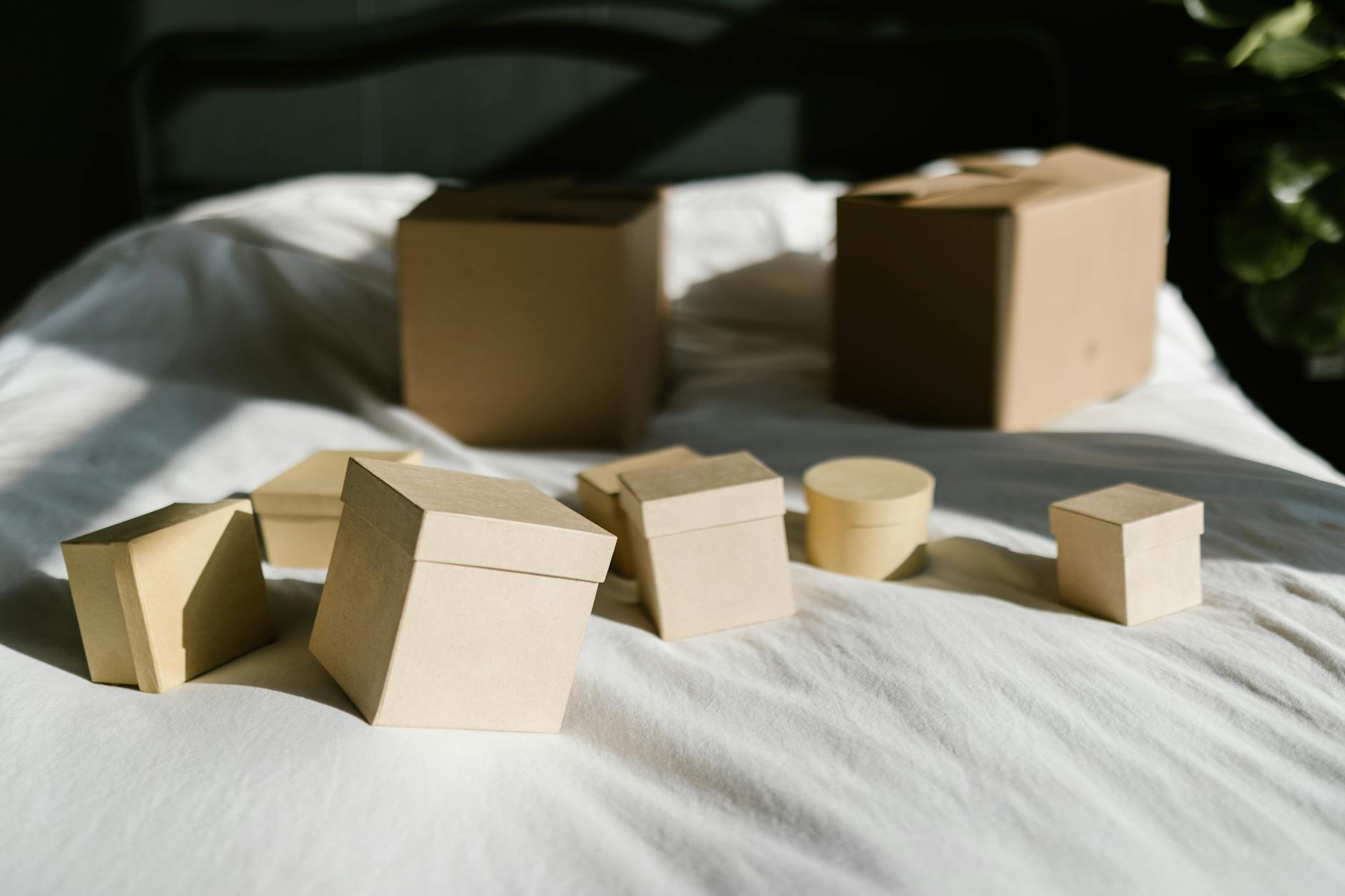 Cardboard boxes with lids arranged on a sunlit bed, casting shadows.