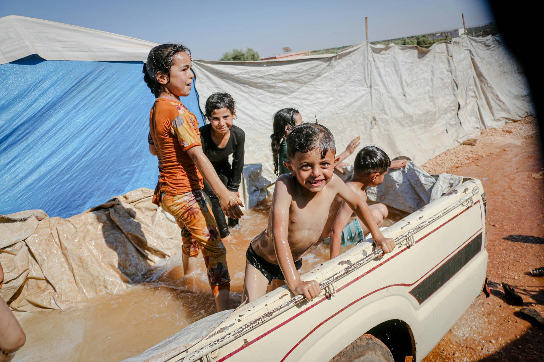 Joyful Syrian children beat the heat by playing in a makeshift pool in Idlib camp.