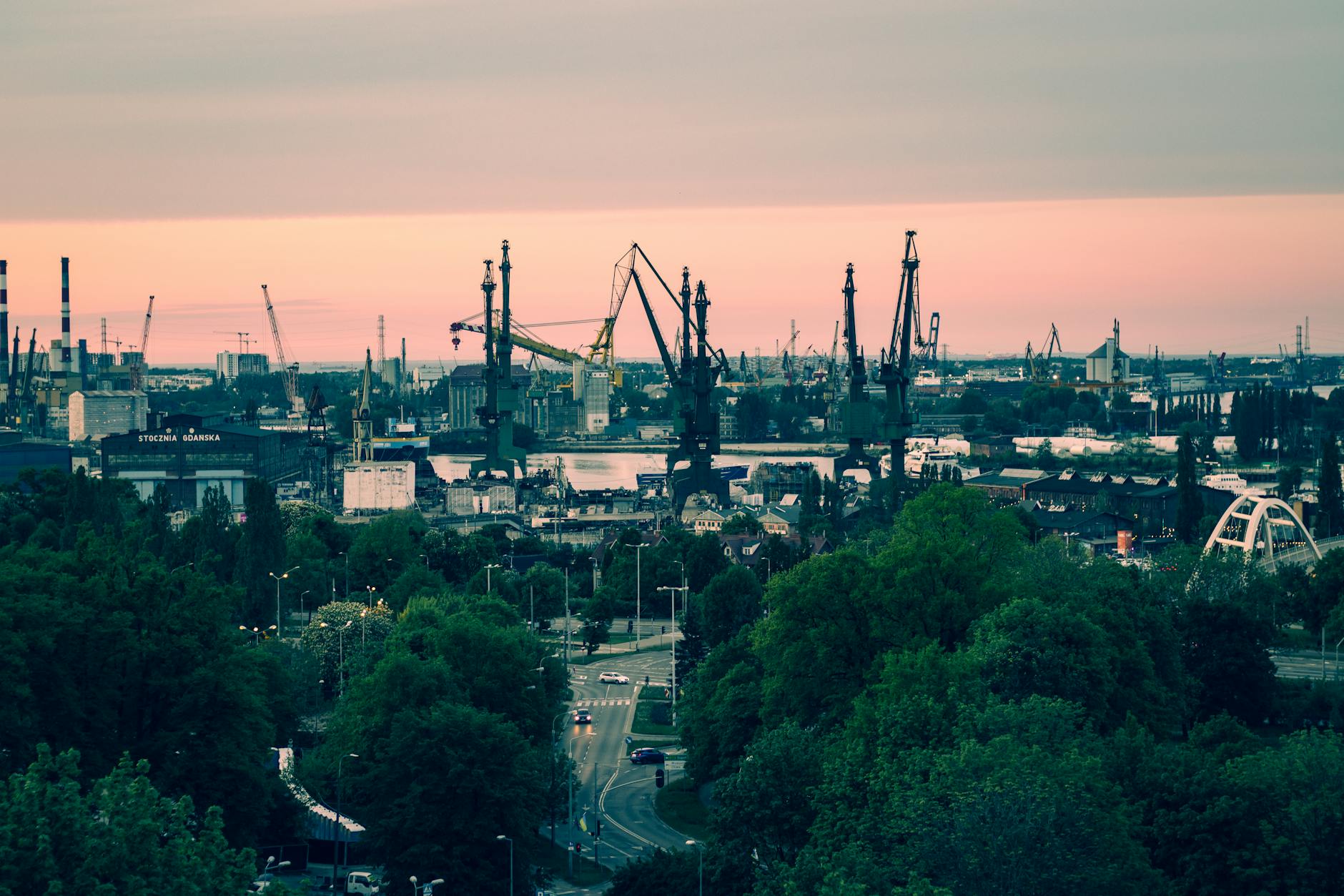 A panoramic view of the iconic Gdańsk shipyard with cranes silhouetted against a vibrant sunset sky.