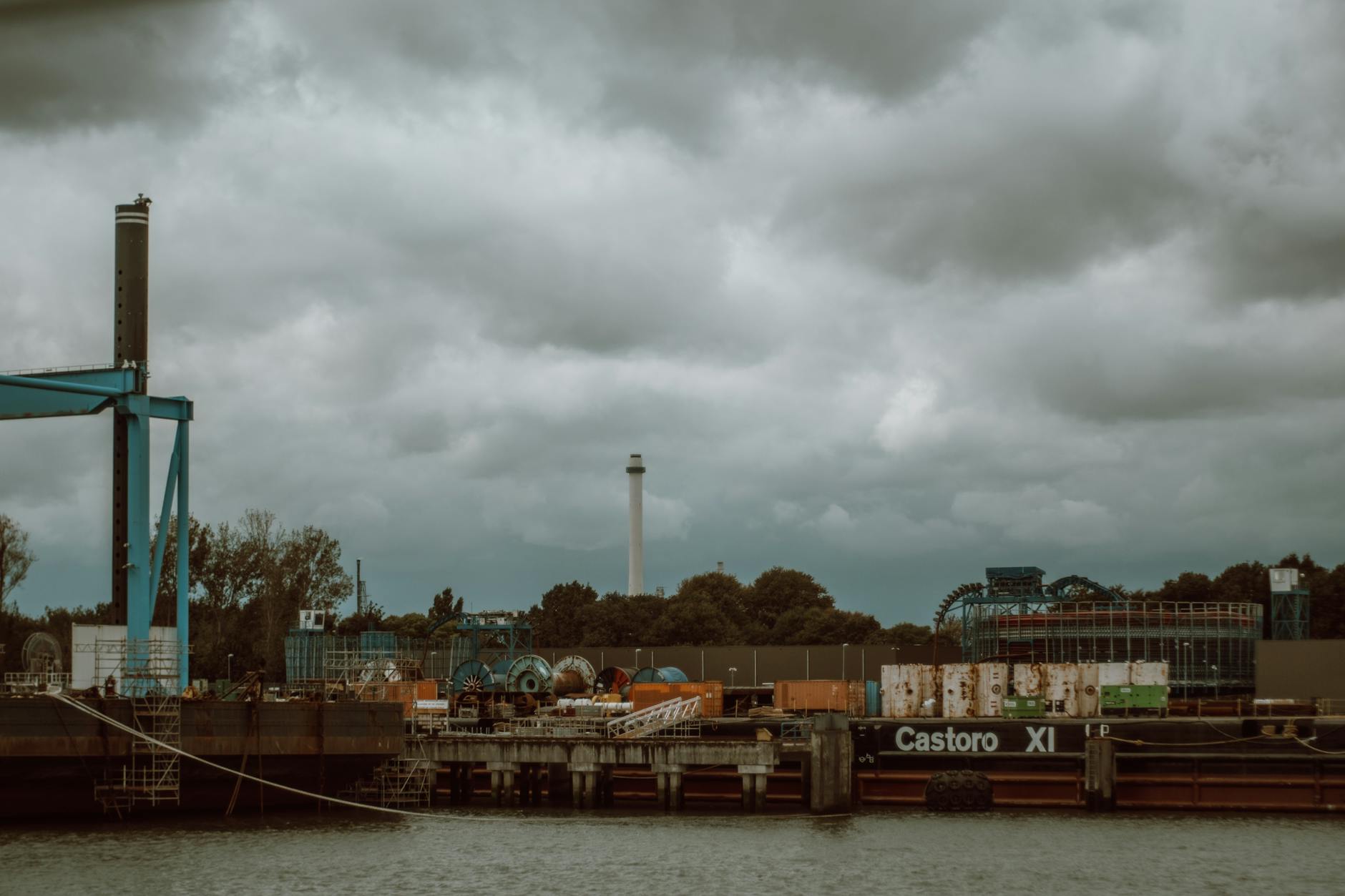 Industrial port of Rotterdam with Castoro XI barge, containers, and equipment against cloudy sky.