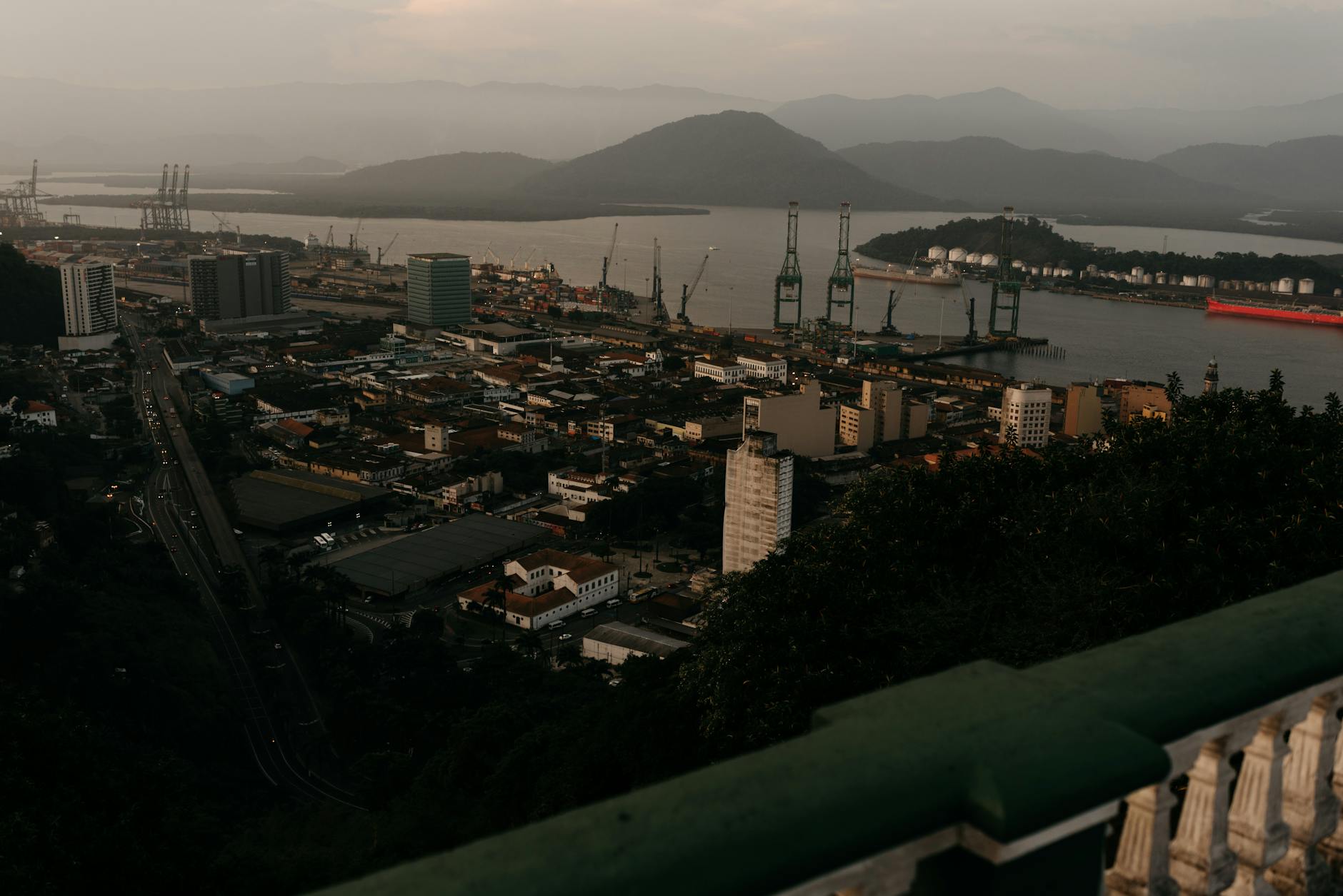 Stunning aerial view of a bustling coastal industrial cityscape during dusk, highlighting docks and cranes.